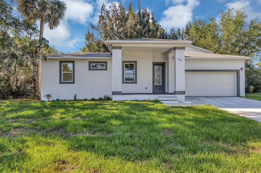A single-story house with a white stucco exterior, a gray front door, and a garage — 1400 CONRAD DRIVE, NEW SMYRNA BEACH, FL