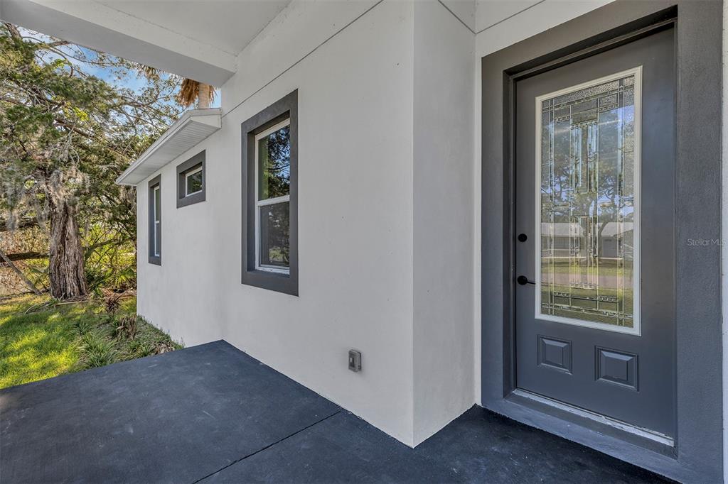 A gray front door with a glass insert sits on a porch beside white walls — 1400 CONRAD DRIVE, NEW SMYRNA BEACH, FL