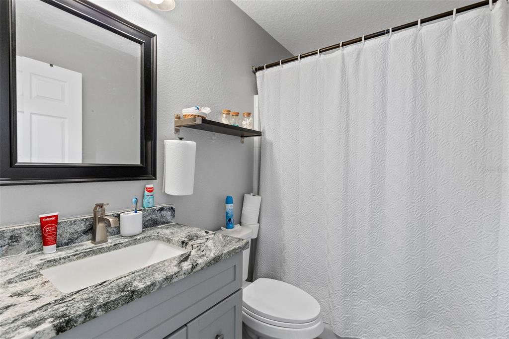 A bathroom features a gray vanity with a granite countertop, a mirror, and a shower curtain — 1214 STILLWATER AVENUE, DELTONA, FL