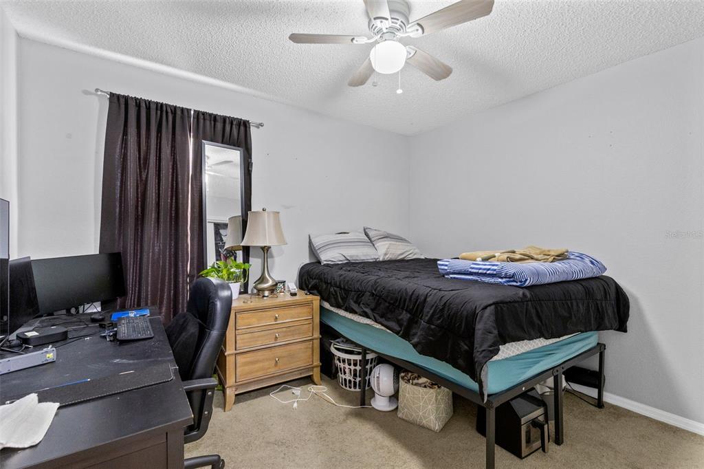 A bedroom features a bed, a desk with a computer, and a wooden nightstand — 1214 STILLWATER AVENUE, DELTONA, FL