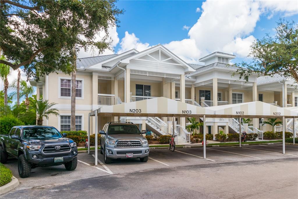 A two-story apartment building features covered parking spaces labeled with unit numbers — 3705 54TH DRIVE W UNIT 103, BRADENTON, FL