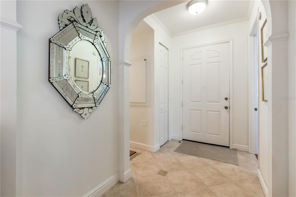 An entryway features a decorative wall mirror, tiled flooring, and a white front door — 3705 54TH DRIVE W UNIT 103, BRADENTON, FL