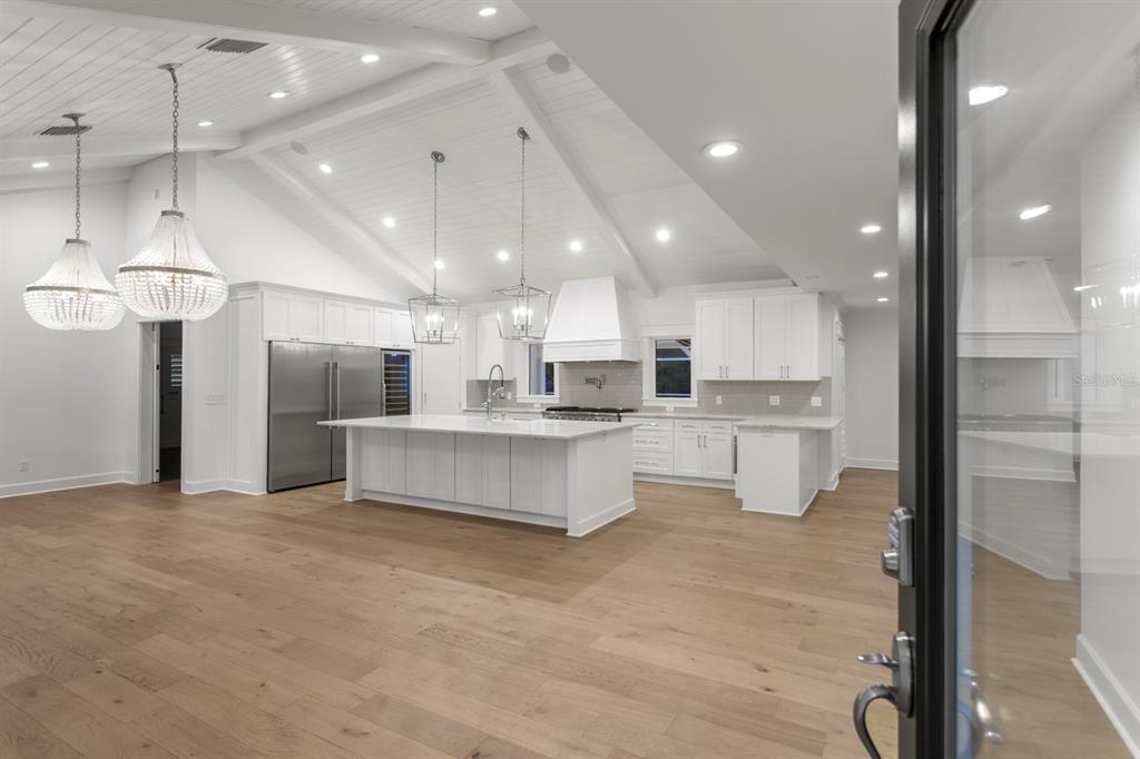 A bright, open-concept kitchen features white cabinetry, a large island, and light wood flooring — 4415 W CLEAR AVENUE, TAMPA, FL