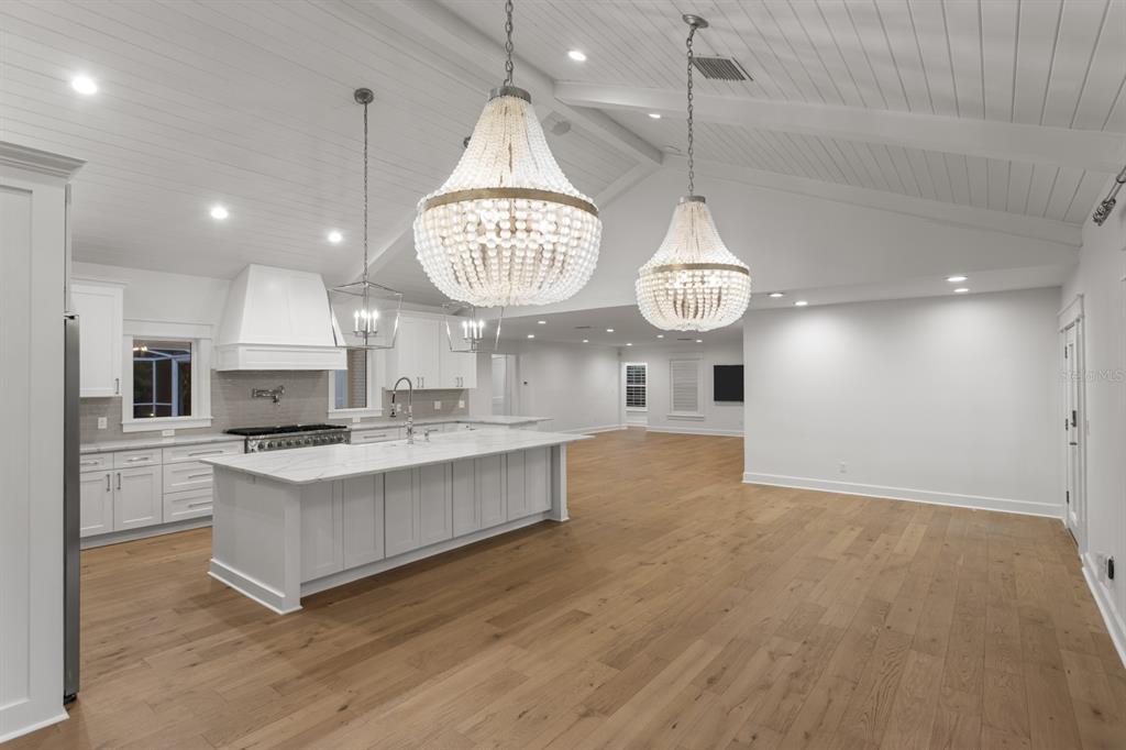 A bright, open-concept kitchen features a large white island, bead chandeliers, and light wood floors — 4415 W CLEAR AVENUE, TAMPA, FL
