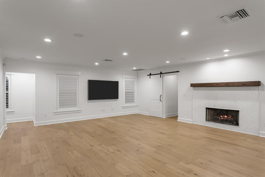 A living room features light wood flooring, a fireplace with a wood mantel, and a television — 4415 W CLEAR AVENUE, TAMPA, FL