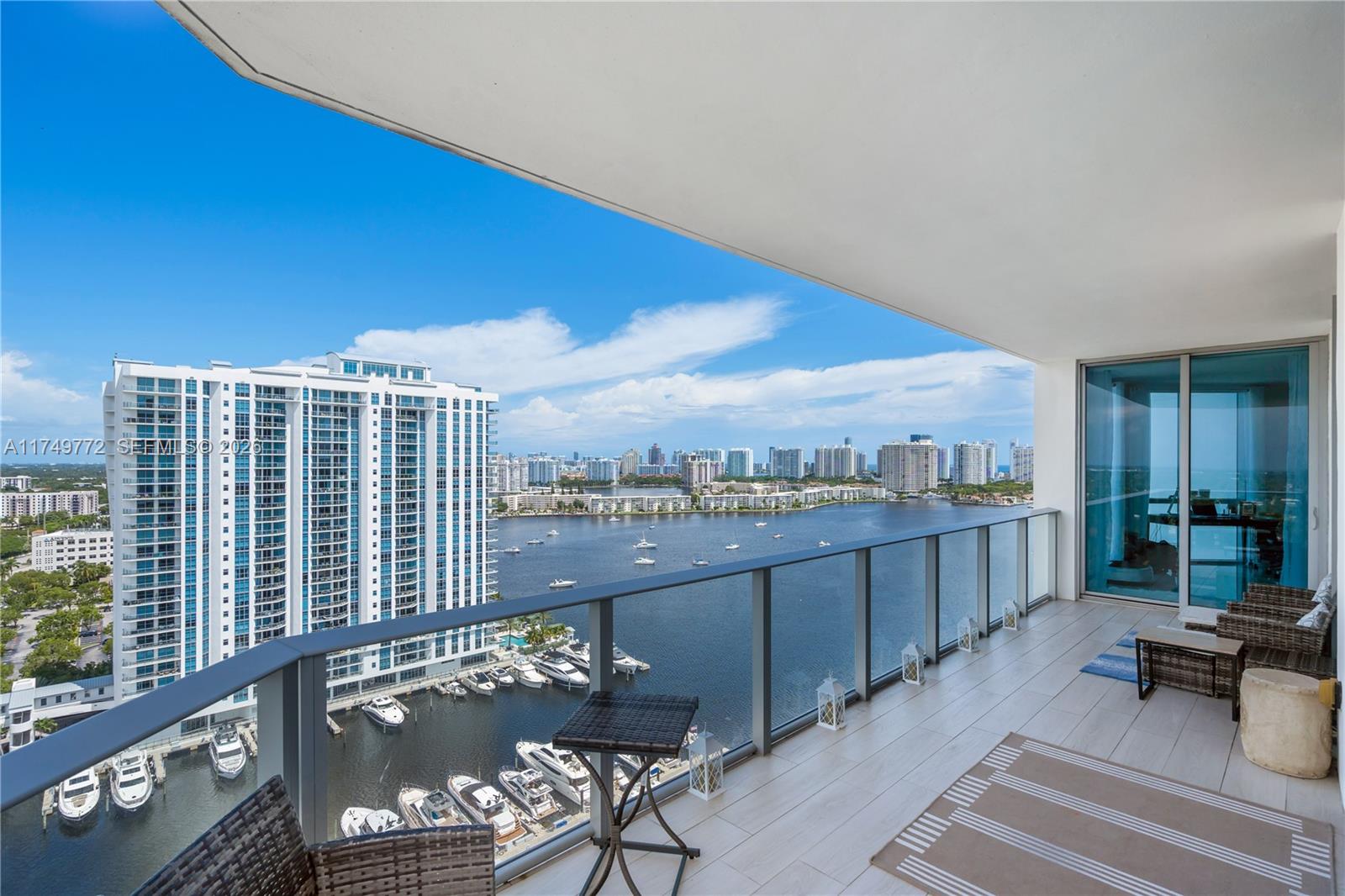 A balcony with outdoor furniture overlooks a marina, a large apartment building, and a bay — 17111 Biscayne Blvd # 2001, North Miami Beach FL 33160, NORTH MIAMI BEACH, FL