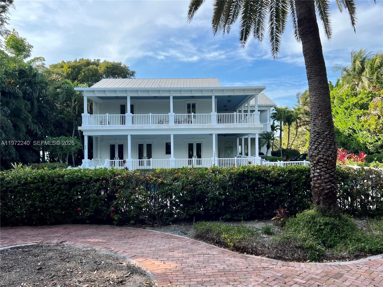 A two-story white house with wrap-around porches stands behind a brick walkway and hedges — 20 Avacado St, Islamorada FL 33036, ISLAMORADA, FL
