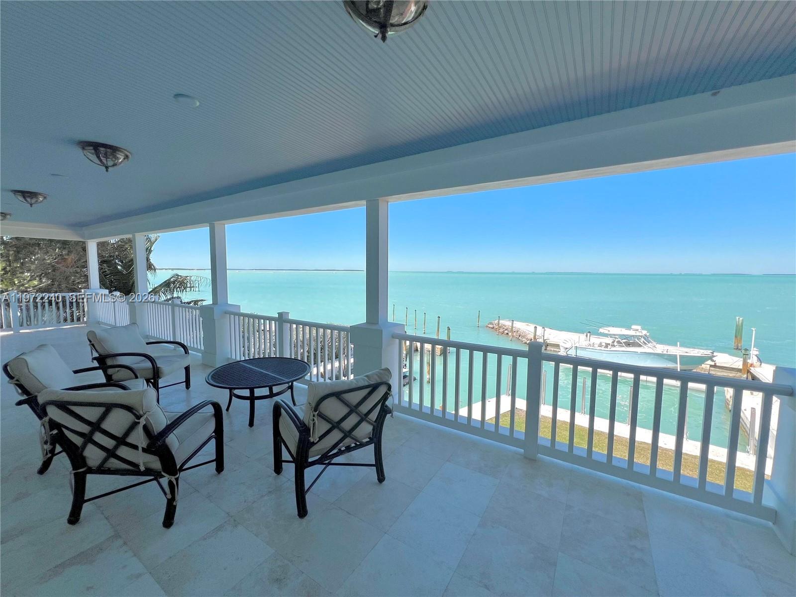 A covered balcony features outdoor seating, white railings, and a view of the ocean — 20 Avacado St, Islamorada FL 33036, ISLAMORADA, FL