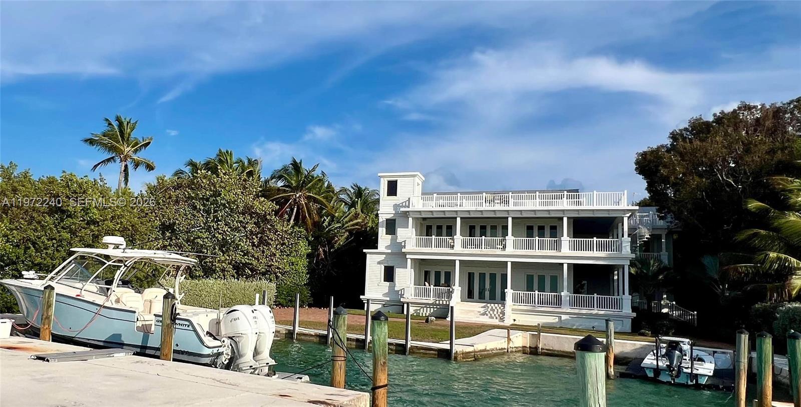 A white three-story house sits on a waterfront lot with two boats docked nearby — 20 Avacado St, Islamorada FL 33036, ISLAMORADA, FL