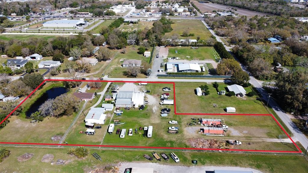 An aerial view shows a large, fenced-in lot containing several buildings, a pond, and multiple vehicles — 2601 11TH AVENUE SE, RUSKIN, FL
