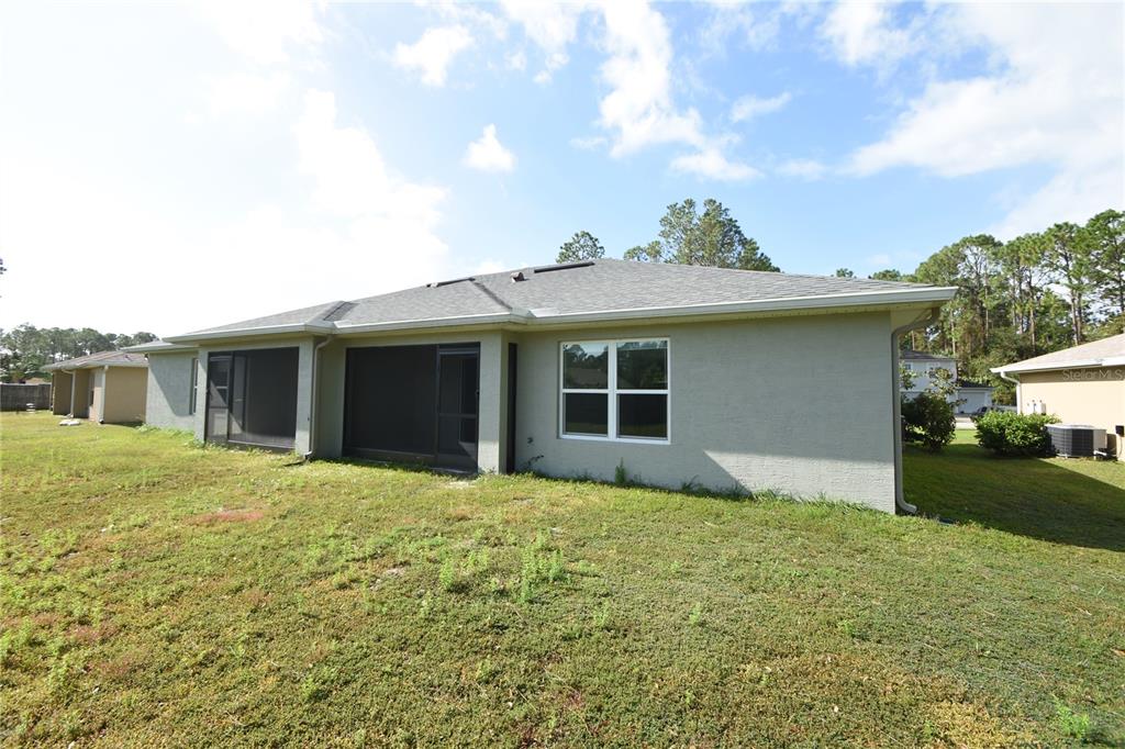 The rear exterior of a single-story house features a screened-in porch and a grassy yard — 77 SEA TRAIL, PALM COAST, FL