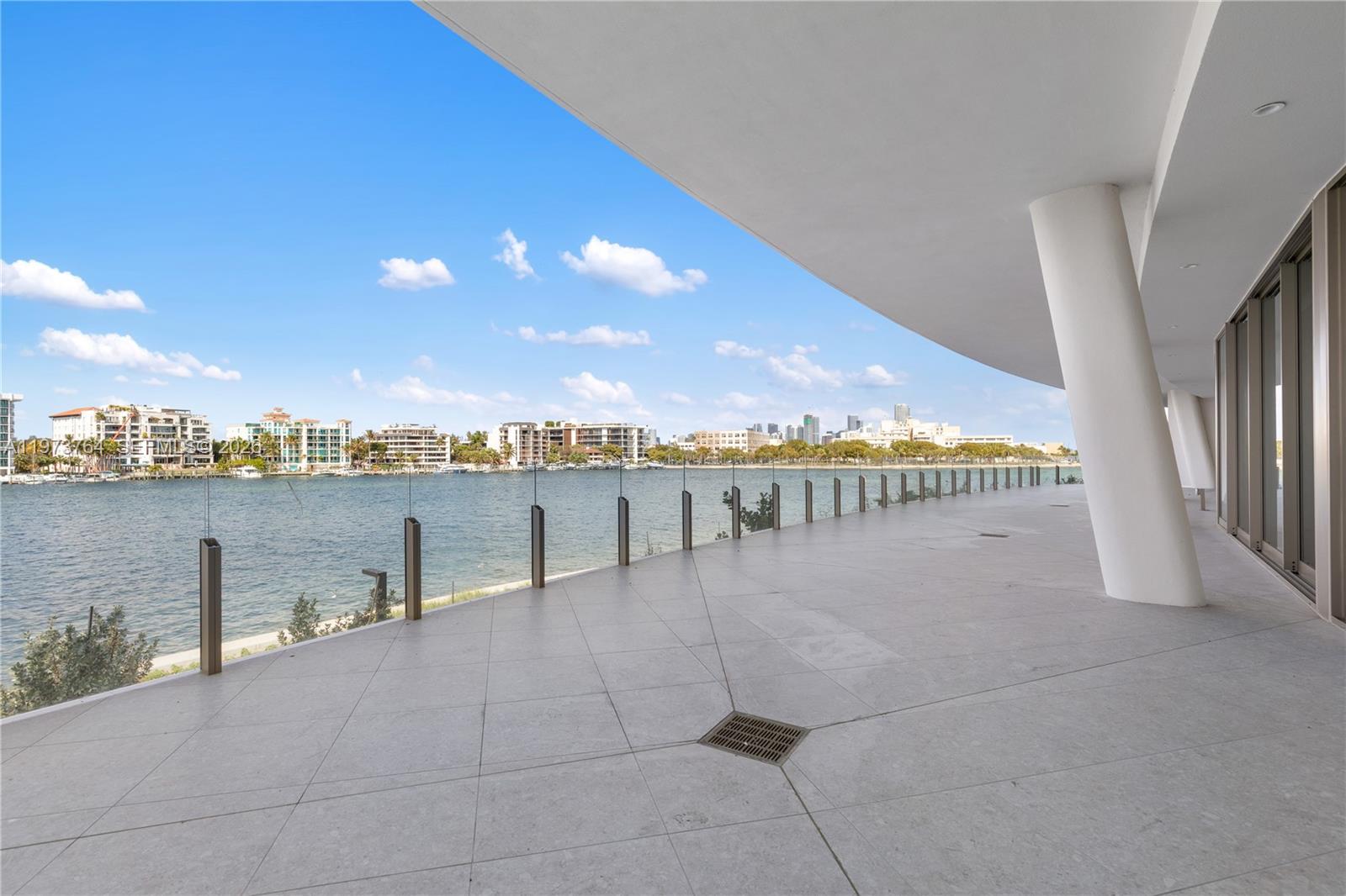A spacious, tiled balcony features a glass railing overlooking a bay and city skyline — 5 Grove Isle Dr # S201, Miami FL 33133, MIAMI, FL