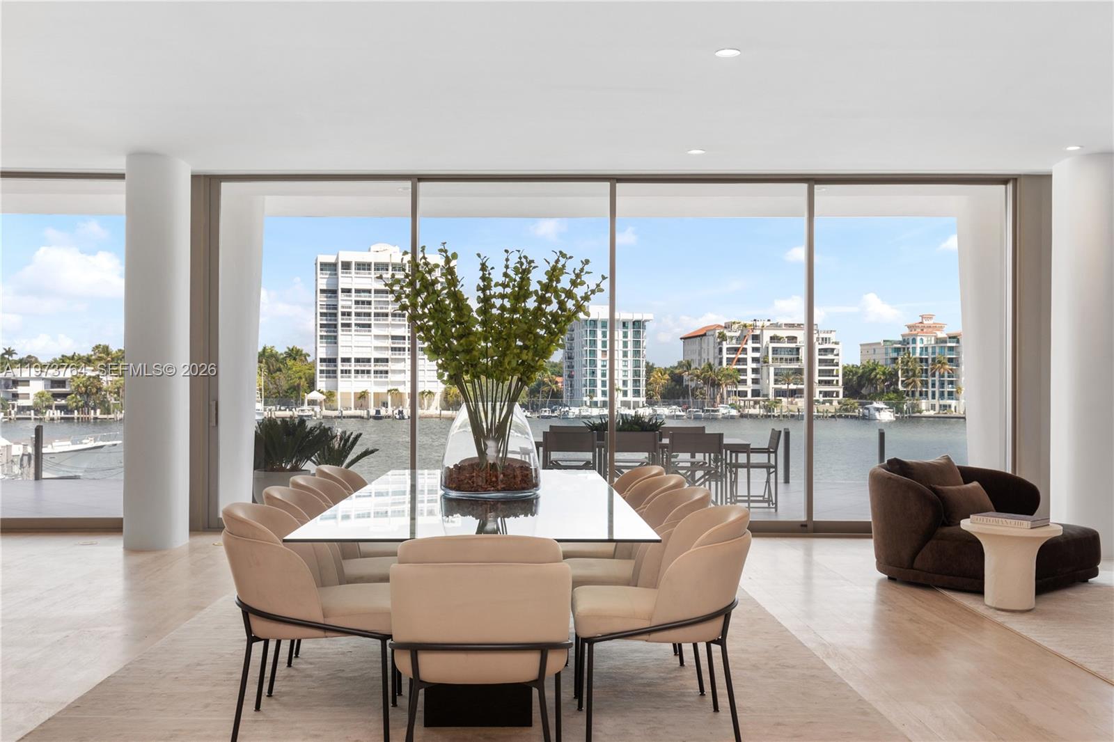 A dining room features a glass table, beige chairs, and floor-to-ceiling windows overlooking a waterway — 5 Grove Isle Dr # S201, Miami FL 33133, MIAMI, FL
