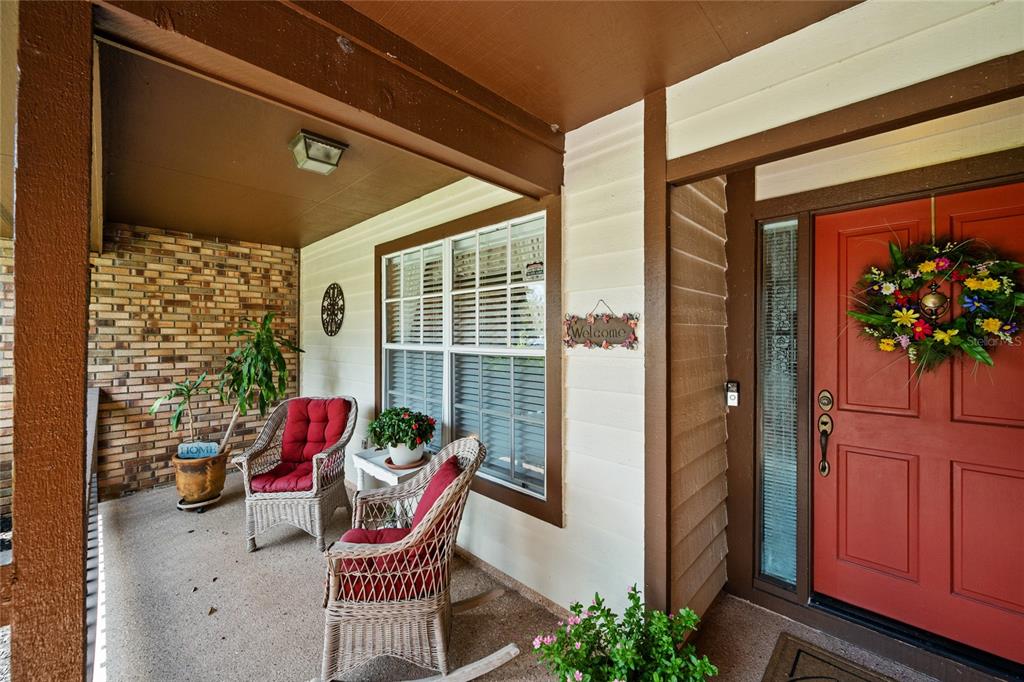 A covered front porch features a red door, two wicker chairs, and a brick wall — 638 WHITE RIVER DRIVE, ORLANDO, FL