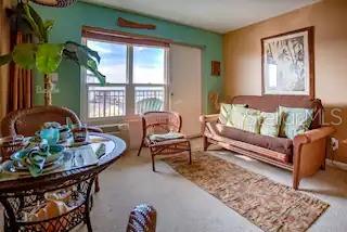 A living room with a brown sofa, a wicker dining set, and a large window — 3727 S ATLANTIC AVENUE UNIT 3150, DAYTONA BEACH, FL