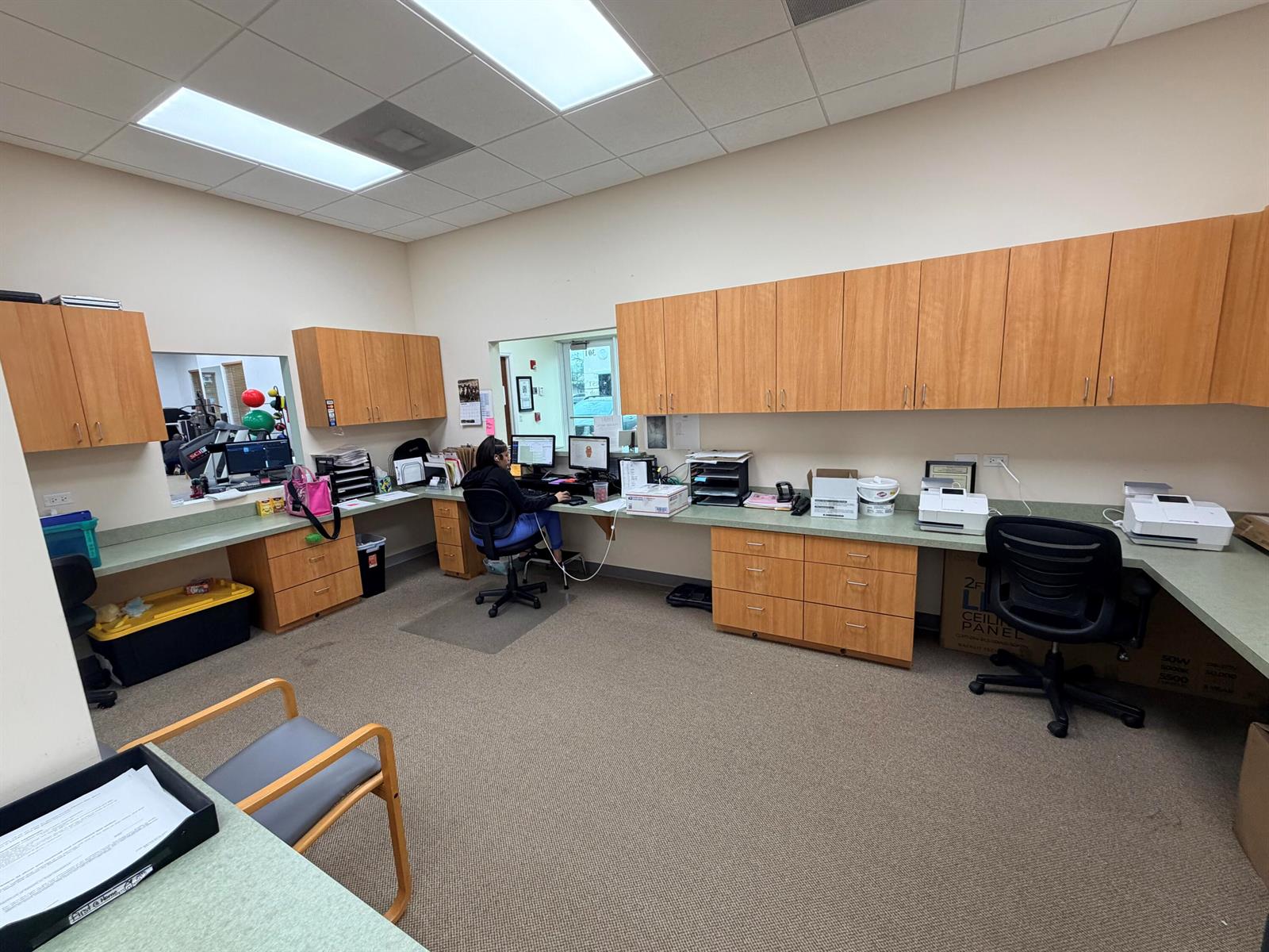 An office space features light wood cabinetry, green countertops, carpeted flooring, and a person working — 5055 S Congress Avenue # 304, Atlantis FL 33461, ATLANTIS, FL