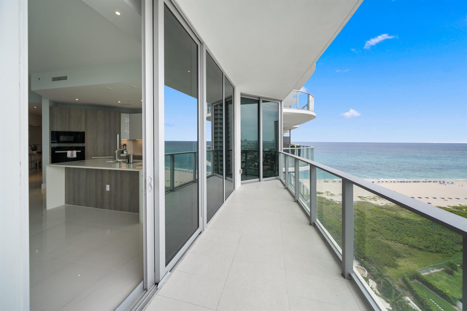 A modern balcony with glass railings overlooks the ocean, adjacent to an indoor kitchen area — 3100 N Ocean Drive # 1608, Singer Island FL 33404, SINGER ISLAND, FL