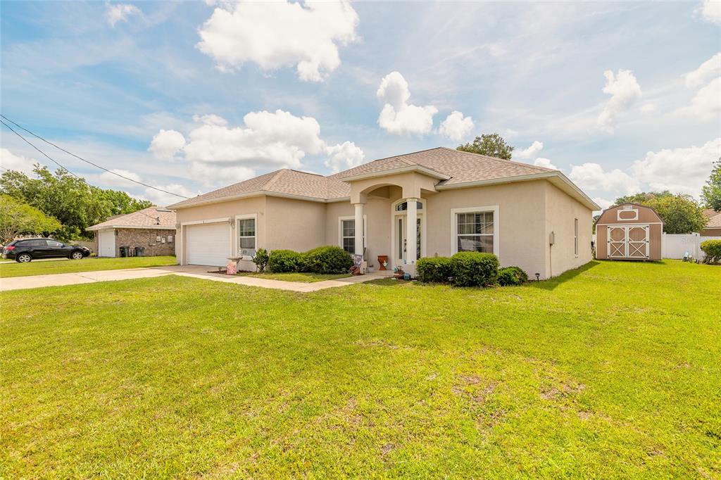 A single-story beige stucco house with a two-car garage and a backyard storage shed — 8 LAMOYNE LANE, PALM COAST, FL