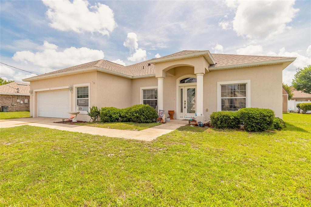 A single-story beige stucco house with a two-car garage and a covered front entryway — 8 LAMOYNE LANE, PALM COAST, FL