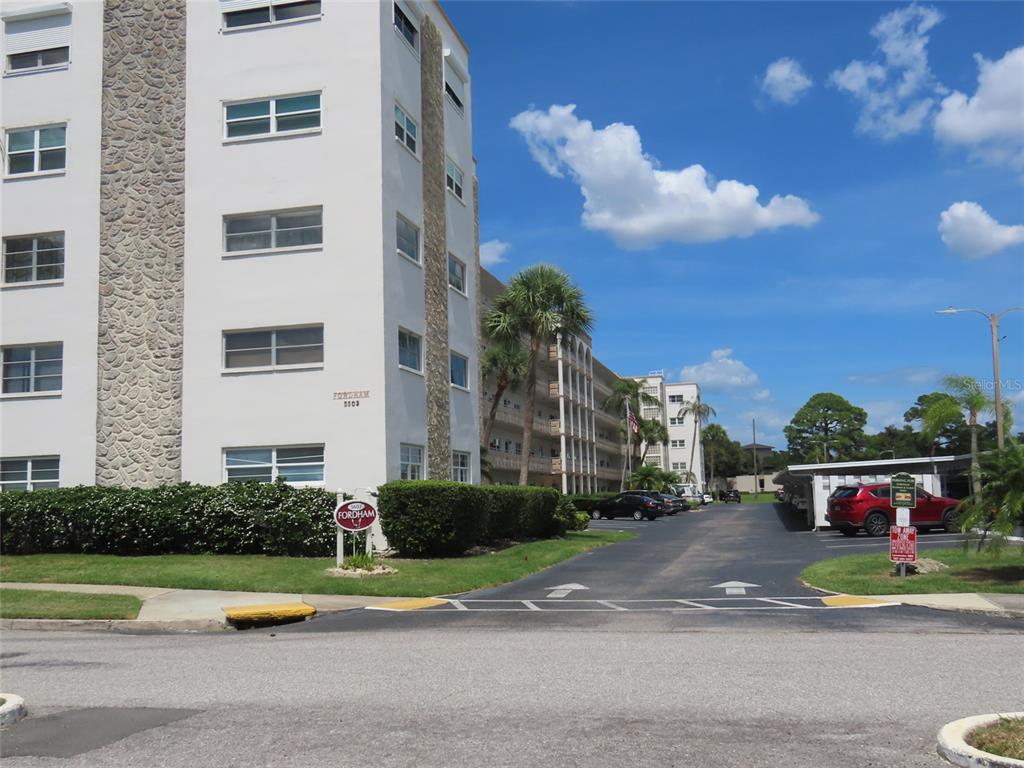 A multi-story apartment building with stone accents stands beside a parking lot and palm trees — 5603 80TH STREET N UNIT 207, ST PETERSBURG, FL