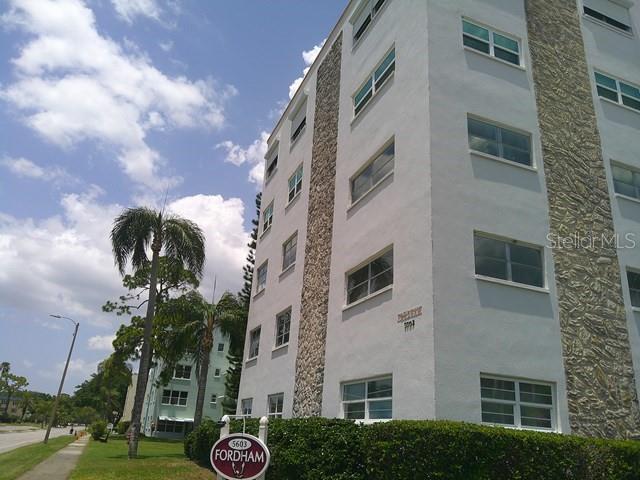 A multi-story apartment building with white stucco walls and stone accents stands near palm trees — 5603 80TH STREET N UNIT 207, ST PETERSBURG, FL