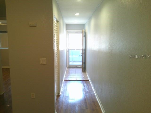 A hallway with wood flooring leads to a glass door opening onto a tiled balcony — 5603 80TH STREET N UNIT 207, ST PETERSBURG, FL