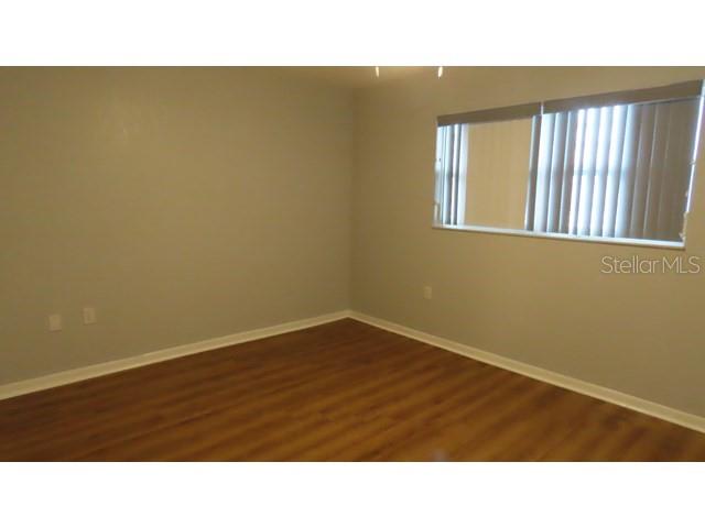 An empty room features light gray walls, wood-look flooring, and a window with vertical blinds — 5603 80TH STREET N UNIT 207, ST PETERSBURG, FL