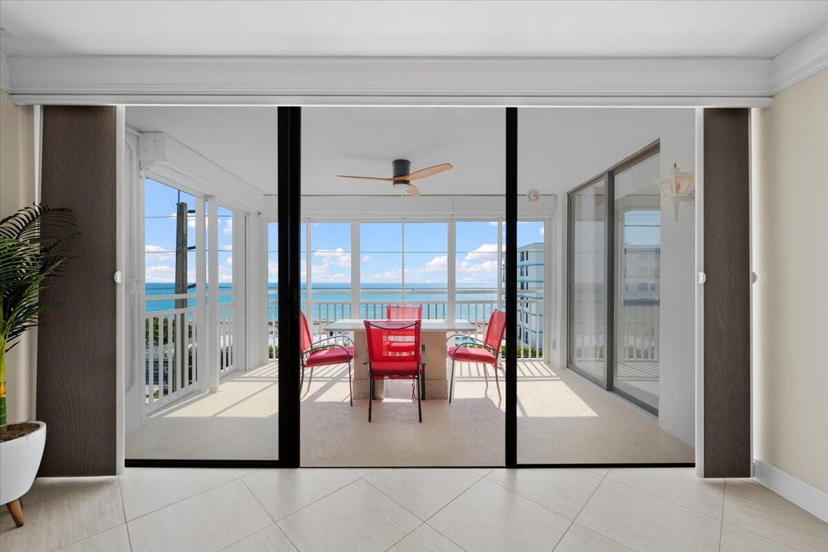 A view through sliding glass doors reveals a balcony with red chairs and ocean views — 911 Ocean Drive # 506, North Palm Beach FL 33408, NORTH PALM BEACH, FL