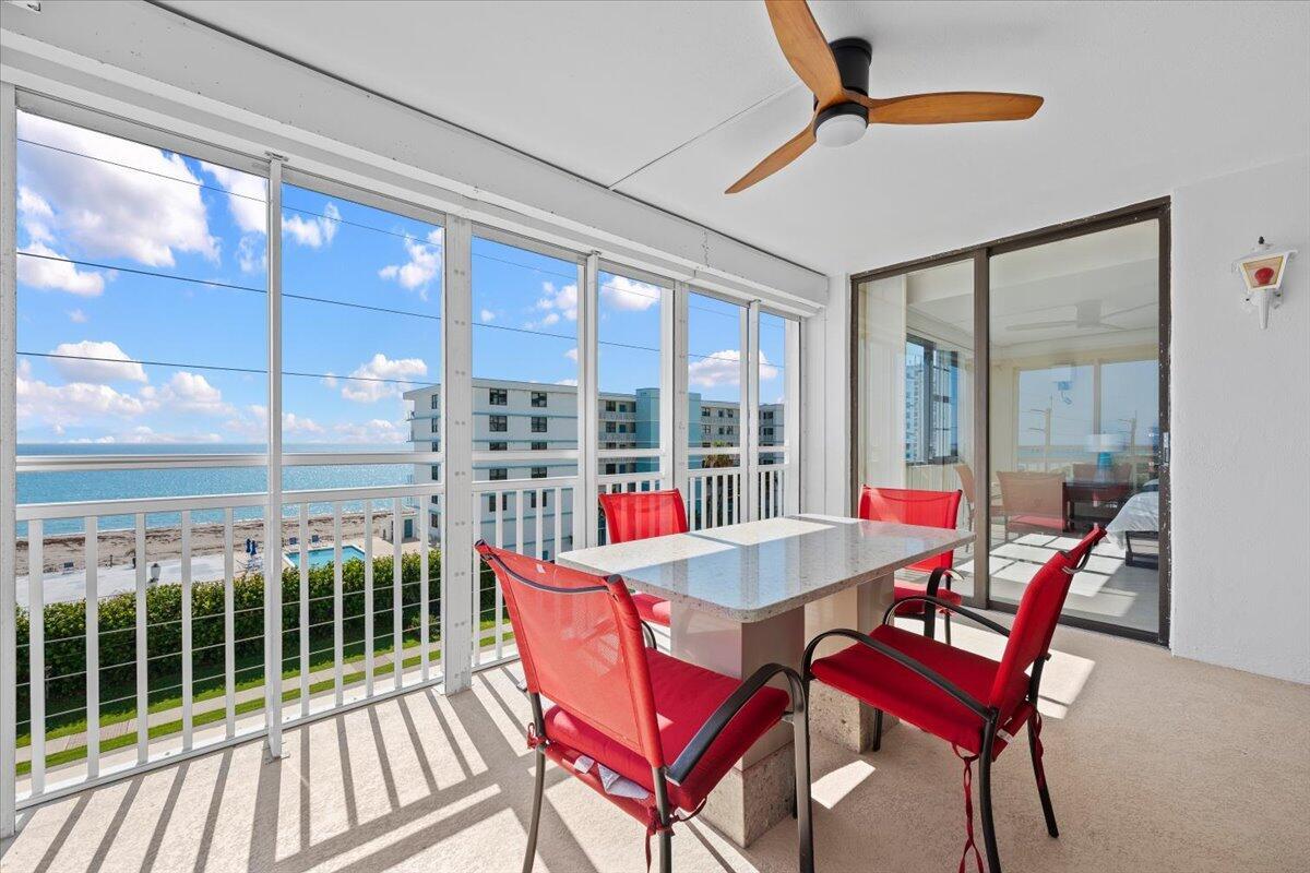 A sunroom with a dining set, ceiling fan, and sliding glass doors overlooking the ocean — 911 Ocean Drive # 506, North Palm Beach FL 33408, NORTH PALM BEACH, FL