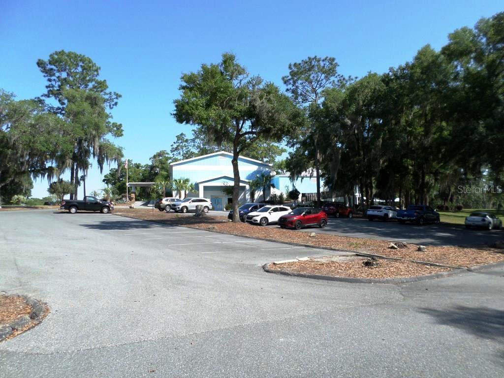 A light blue building sits behind a paved parking lot surrounded by mature trees — 8518 SW 189TH COURT RD, DUNNELLON, FL