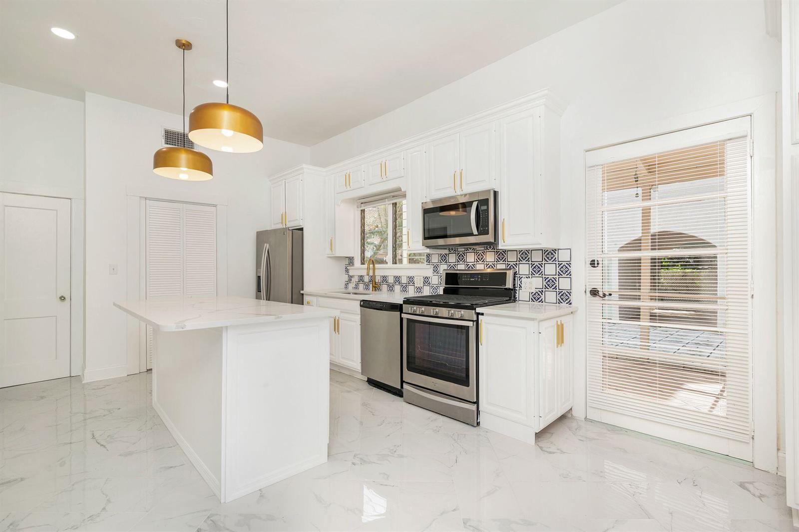 A bright kitchen features white cabinets, marble-look floors, a center island, and patterned tile backsplash — 232 Rugby Road, West Palm Beach FL 33405, WEST PALM BEACH, FL