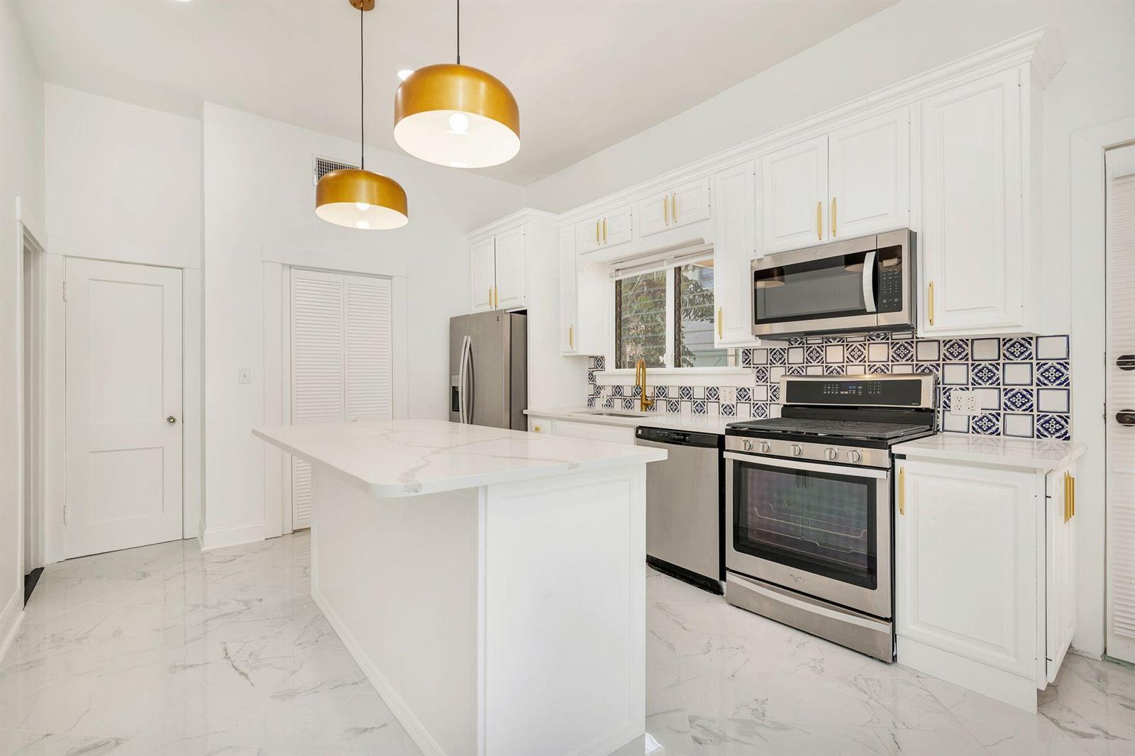 A white kitchen features a marble-topped island, gold pendant lights, and a patterned tile backsplash — 232 Rugby Road, West Palm Beach FL 33405, WEST PALM BEACH, FL