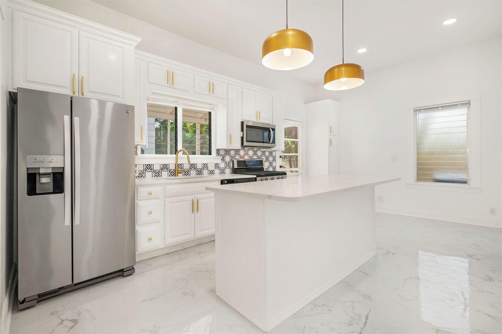 A bright kitchen features white cabinets, a central island, stainless steel appliances, and marble flooring — 232 Rugby Road, West Palm Beach FL 33405, WEST PALM BEACH, FL