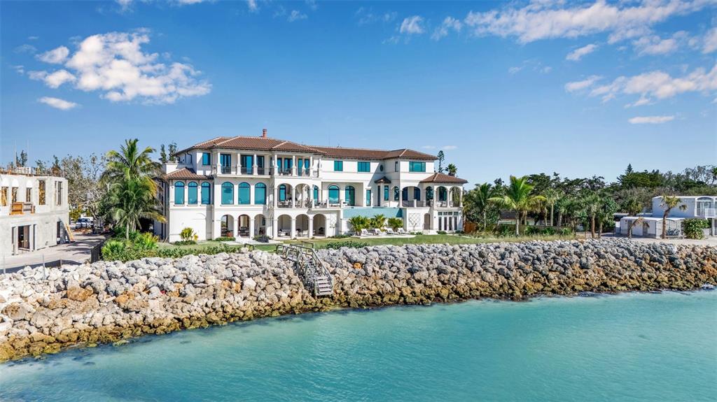 A large, multi-story Mediterranean-style mansion sits behind a rock seawall overlooking turquoise water — 7366 POINT OF ROCKS ROAD, SARASOTA, FL