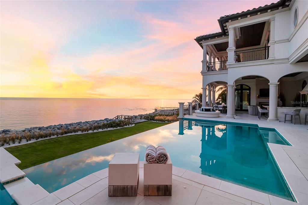 An infinity pool overlooks the ocean from the patio of a multi-story white luxury home — 7366 POINT OF ROCKS ROAD, SARASOTA, FL
