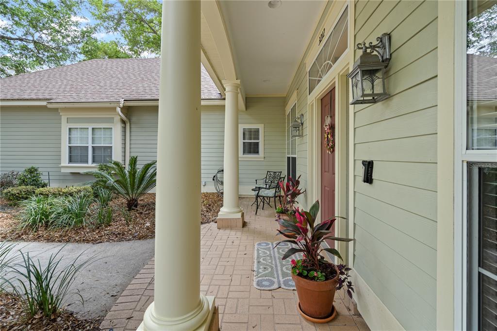 A covered front porch features light green siding, a brick paver floor, and a red door — 3212 SW 98TH DRIVE, GAINESVILLE, FL