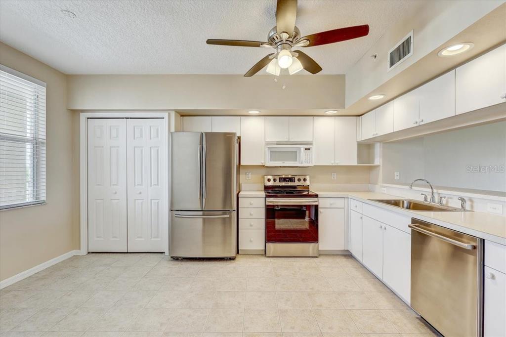 A kitchen features white cabinetry, stainless steel appliances, and light-colored tile flooring — 1200 COUNTRY CLUB DRIVE UNIT 3405, LARGO, FL