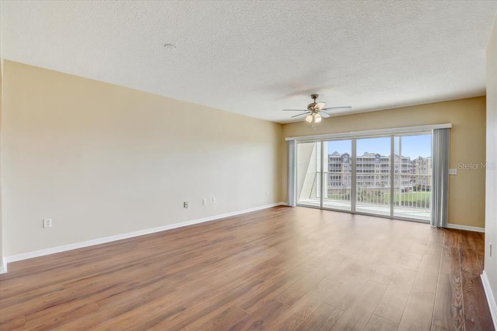 An empty living room features wood-look flooring, a ceiling fan, and sliding glass balcony doors — 1200 COUNTRY CLUB DRIVE UNIT 3405, LARGO, FL