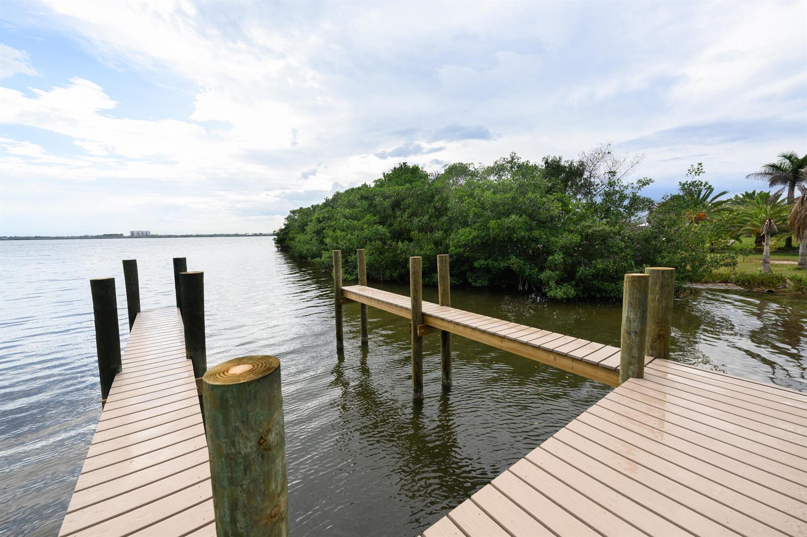 An aerial view shows a wooden dock extending into a bay near a grassy shoreline — 1540 Outer Drive, Merritt Island FL 32952, MERRITT ISLAND, FL