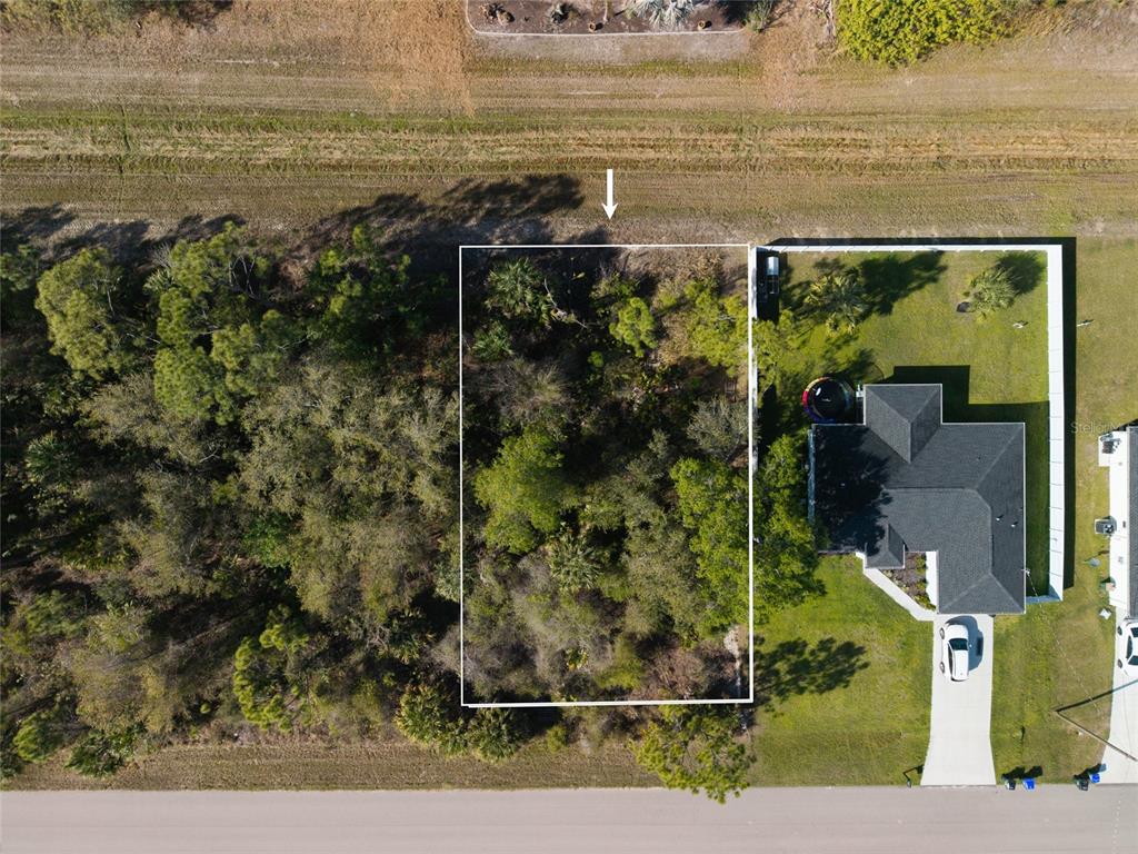 An aerial view shows a rectangular vacant lot situated between a wooded area and a house — Lot 6 SAWYER CIRCLE, NORTH PORT, FL