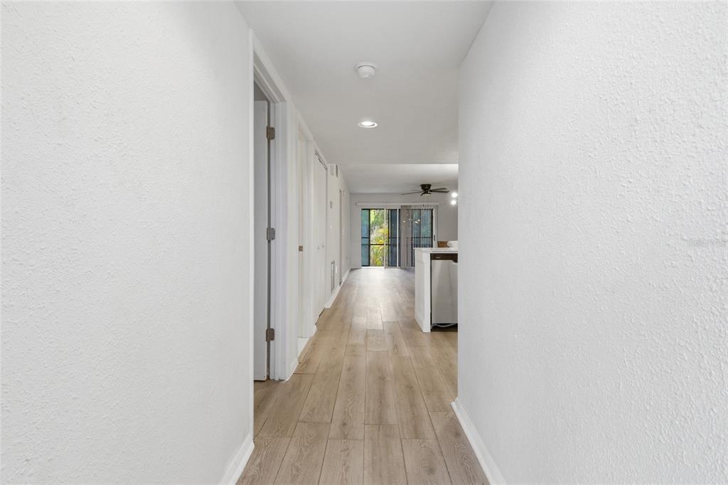 A hallway with light wood-look flooring leads toward an open living area with sliding doors — 6800 PLACIDA ROAD UNIT 132, ENGLEWOOD, FL