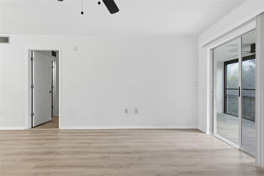 An empty room with light wood-look flooring, white walls, a doorway, and sliding glass doors — 6800 PLACIDA ROAD UNIT 132, ENGLEWOOD, FL