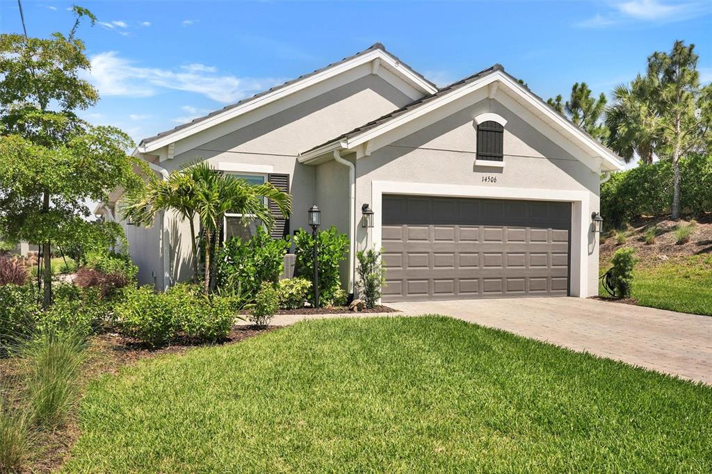 A single-story house with a gray garage door, light-colored stucco walls, and a landscaped yard — 14506 DERNA TERRACE, BRADENTON, FL