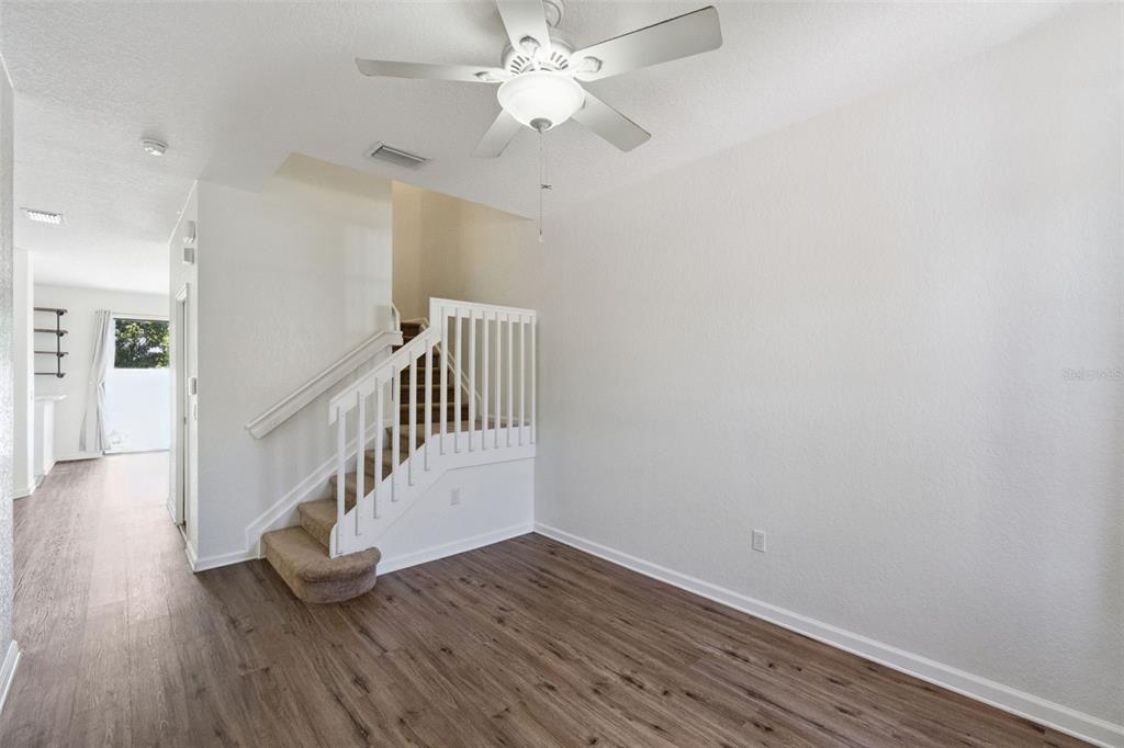 A living area features wood-look flooring, a ceiling fan, and a carpeted staircase with railings — 3491 ALLEGRA CIRCLE, ST CLOUD, FL