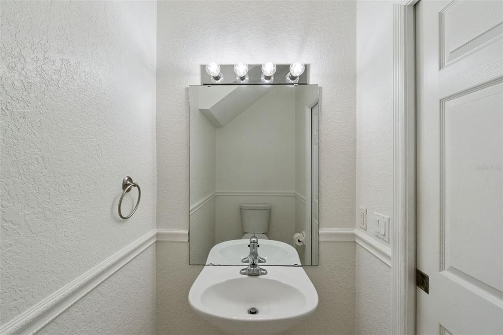A small bathroom features a wall-mounted sink, a mirror, and a four-bulb vanity light — 3491 ALLEGRA CIRCLE, ST CLOUD, FL