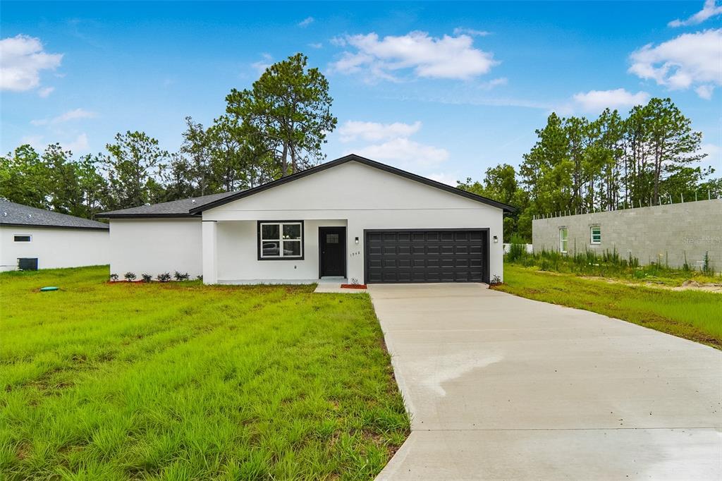 A single-story white house with a black garage door and a concrete driveway — 1948 W ADELIA PLACE, CITRUS SPRINGS, FL