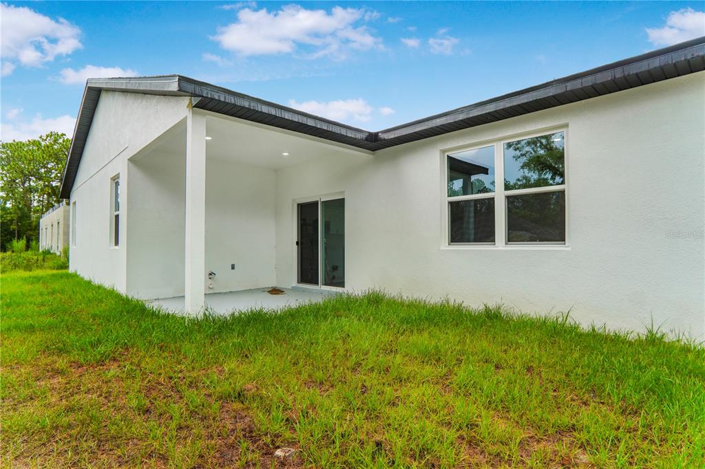 The exterior of a white house features a covered patio and a sliding glass door — 1948 W ADELIA PLACE, CITRUS SPRINGS, FL