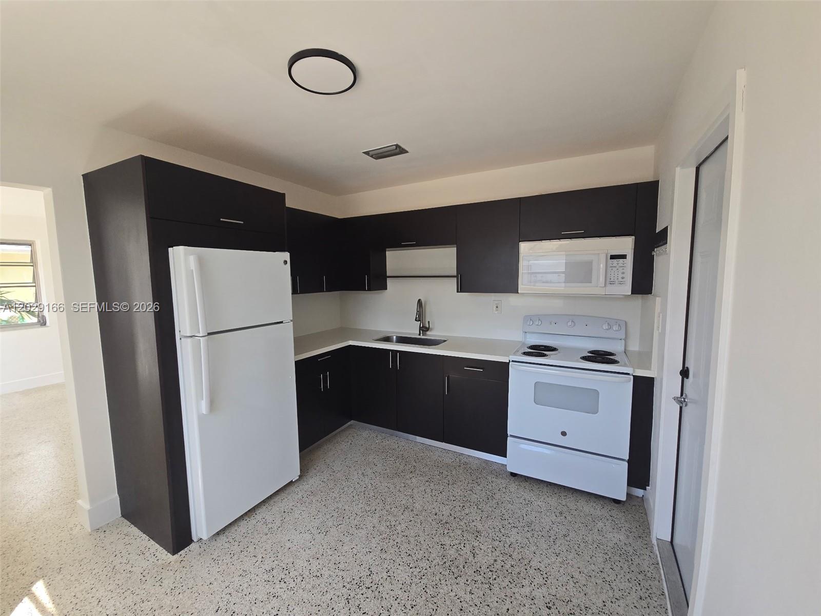 A kitchen features dark brown cabinets, white appliances, and light-colored countertops over speckled flooring — 3435 NW 4th St, Miami FL 33125, MIAMI, FL