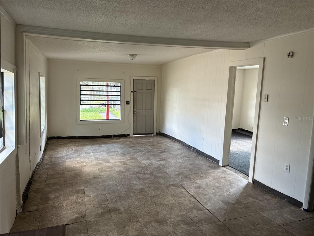 An empty room features tiled flooring, white paneled walls, a front door, and a window — 10529 3RD AVENUE, OCOEE, FL