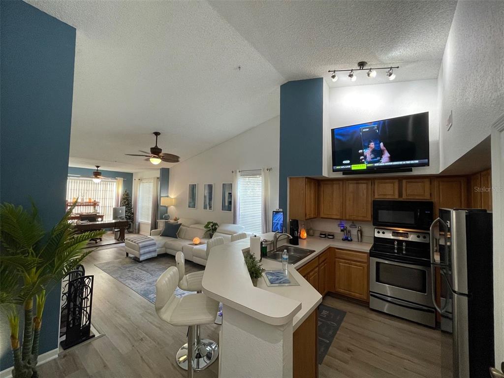 An open-concept kitchen with wood cabinets and a breakfast bar overlooks a living room area — 13103 MULBERRY PARK DRIVE UNIT 831, ORLANDO, FL